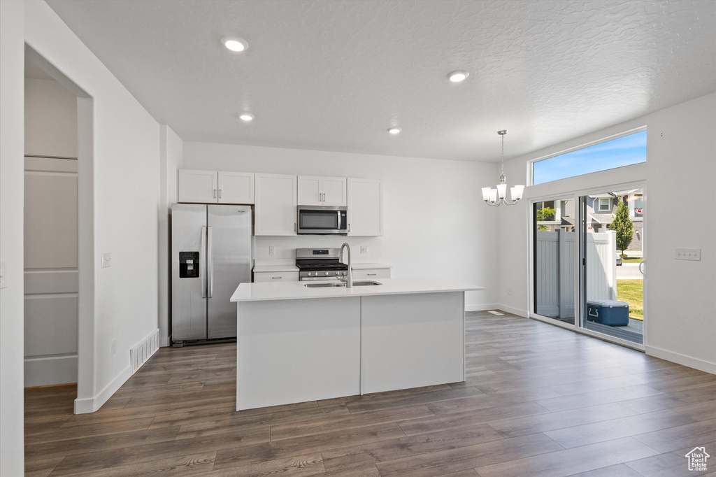 Kitchen with appliances with stainless steel finishes, a chandelier, white cabinets, a kitchen island with sink, and dark wood-style flooring