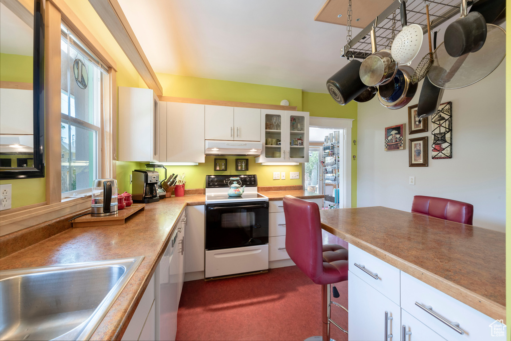 Kitchen with white appliances, under cabinet range hood, white cabinetry, glass insert cabinets, and a kitchen bar