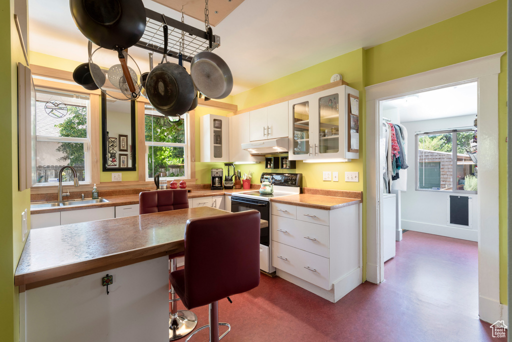 Kitchen with range with electric cooktop, under cabinet range hood, white cabinets, and glass insert cabinets