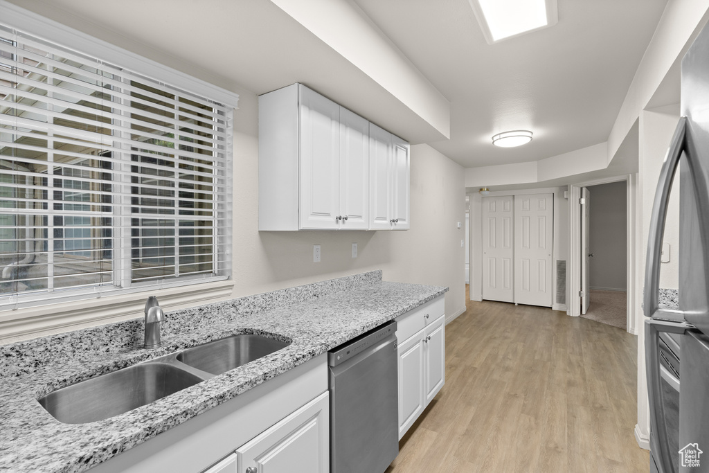 Kitchen with stainless steel appliances, light wood finished floors, white cabinets, and light stone countertops