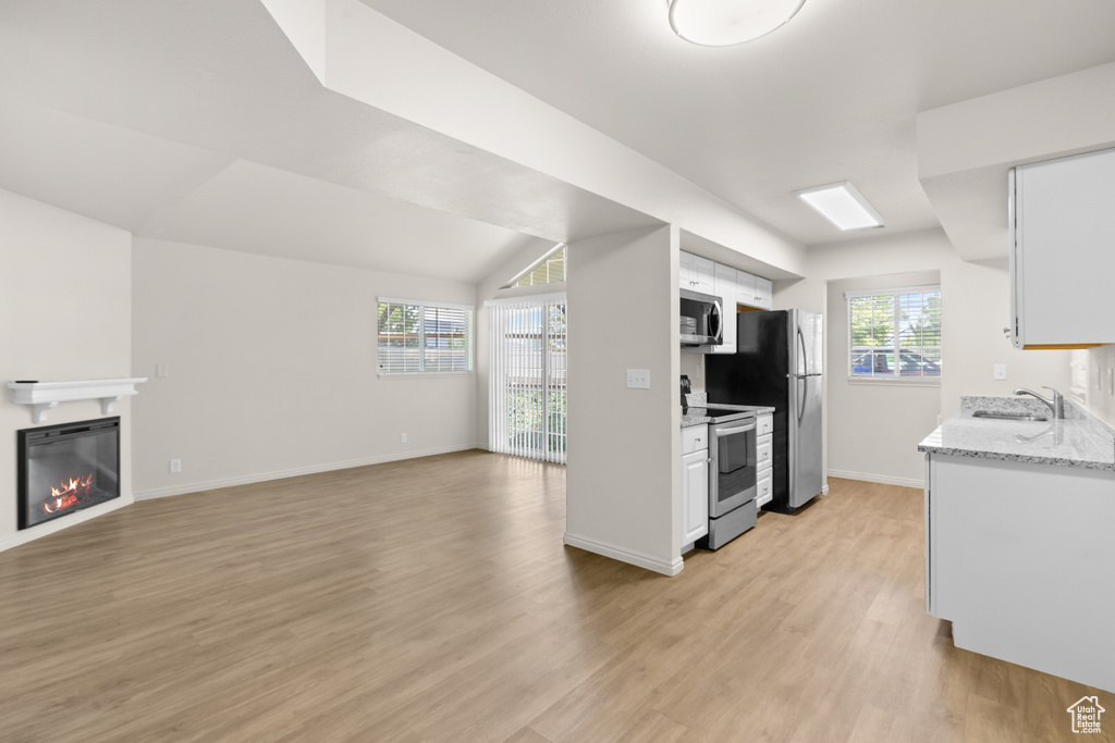 Kitchen with stainless steel appliances, light wood-style floors, white cabinets, a glass covered fireplace, and open floor plan