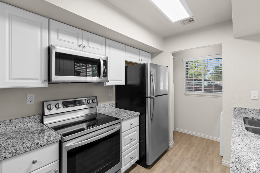Kitchen with stainless steel appliances, light wood-type flooring, white cabinets, and light stone countertops