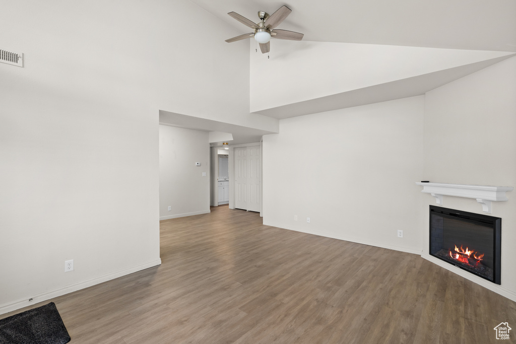 Unfurnished living room featuring a glass covered fireplace, wood finished floors, ceiling fan, and high vaulted ceiling