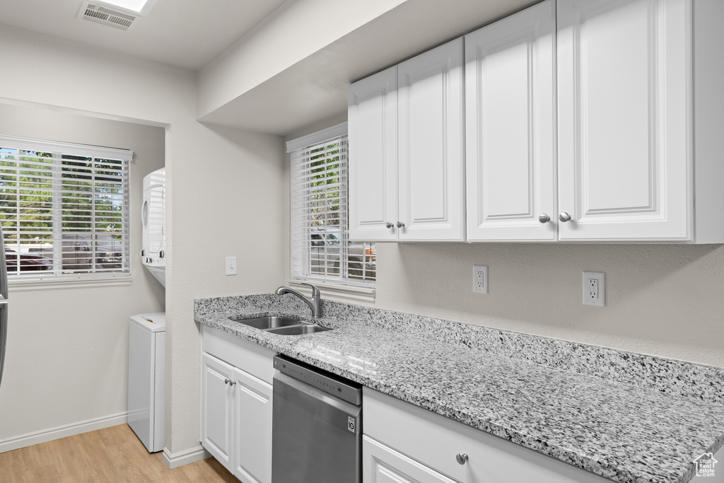 Kitchen with stainless steel dishwasher, light wood finished floors, white cabinets, and light stone countertops