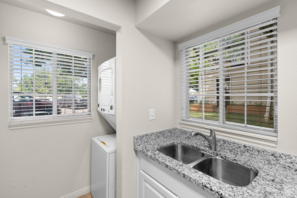 Laundry room featuring stacked washer / drying machine, plenty of natural light, and cabinet space