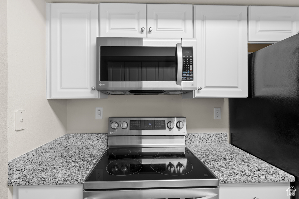 Kitchen with appliances with stainless steel finishes, white cabinets, and light stone counters