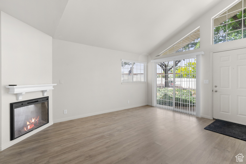 Unfurnished living room with wood finished floors, healthy amount of natural light, a glass covered fireplace, and high vaulted ceiling