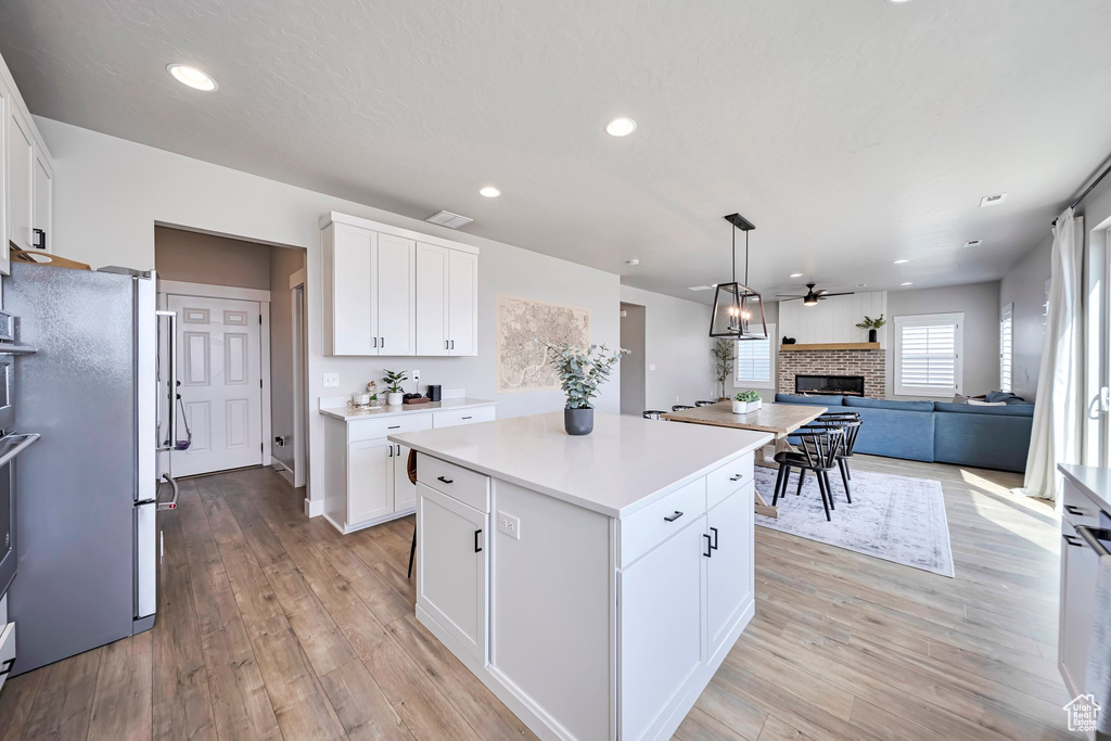 Kitchen with a brick fireplace, light wood finished floors, open floor plan, light countertops, and ceiling fan