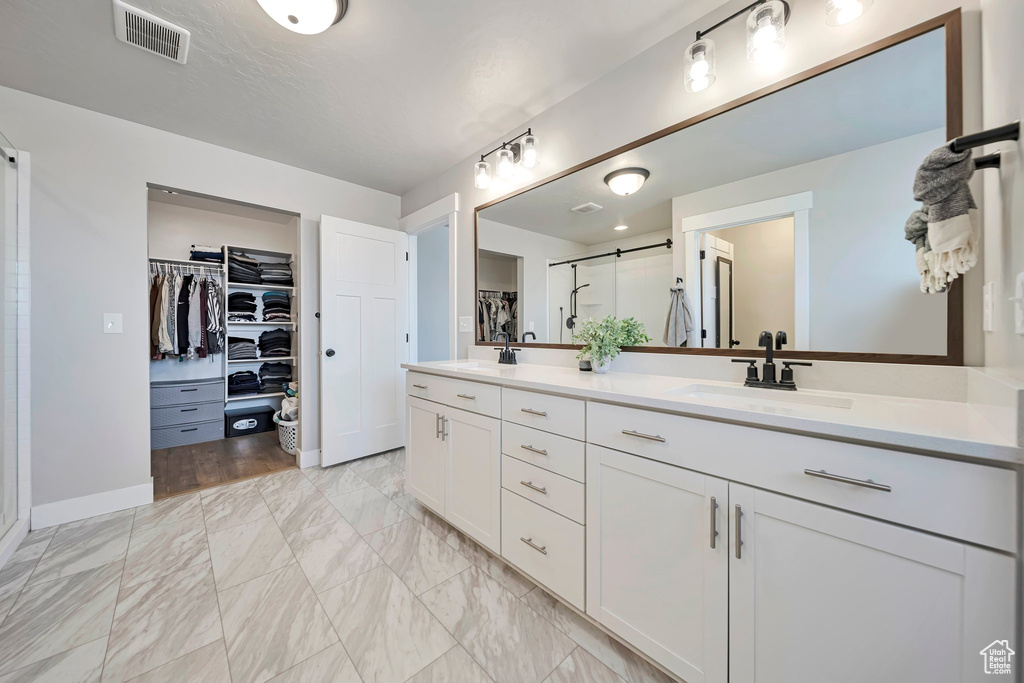 Bathroom with a walk in closet, a stall shower, double vanity, and marble look tiles