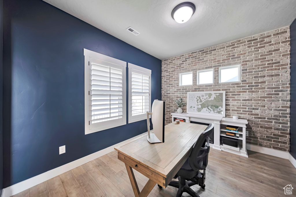 Office with brick wall, an accent wall, and light wood-style floors