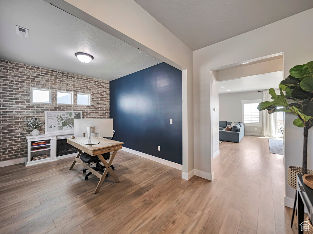 Office featuring brick wall, wood finished floors, and an accent wall