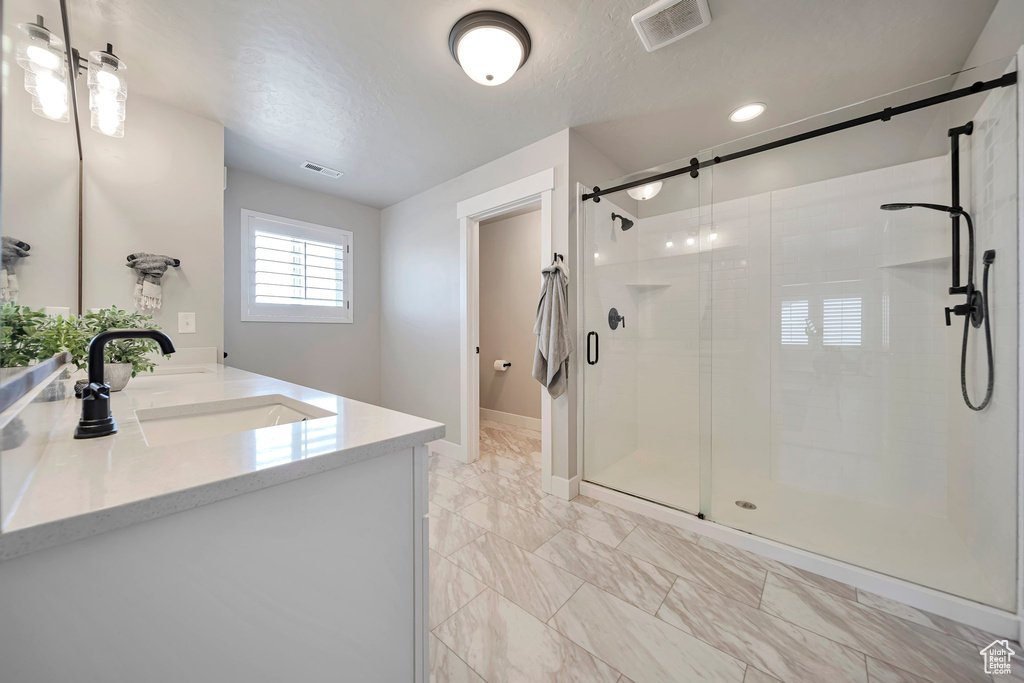 Full bathroom with double vanity, a shower stall, marble look tile flooring, and a textured ceiling