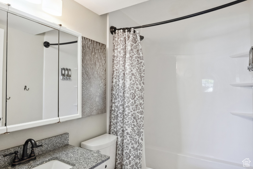 Bathroom featuring toilet, shower / bathtub combination with curtain, and vanity