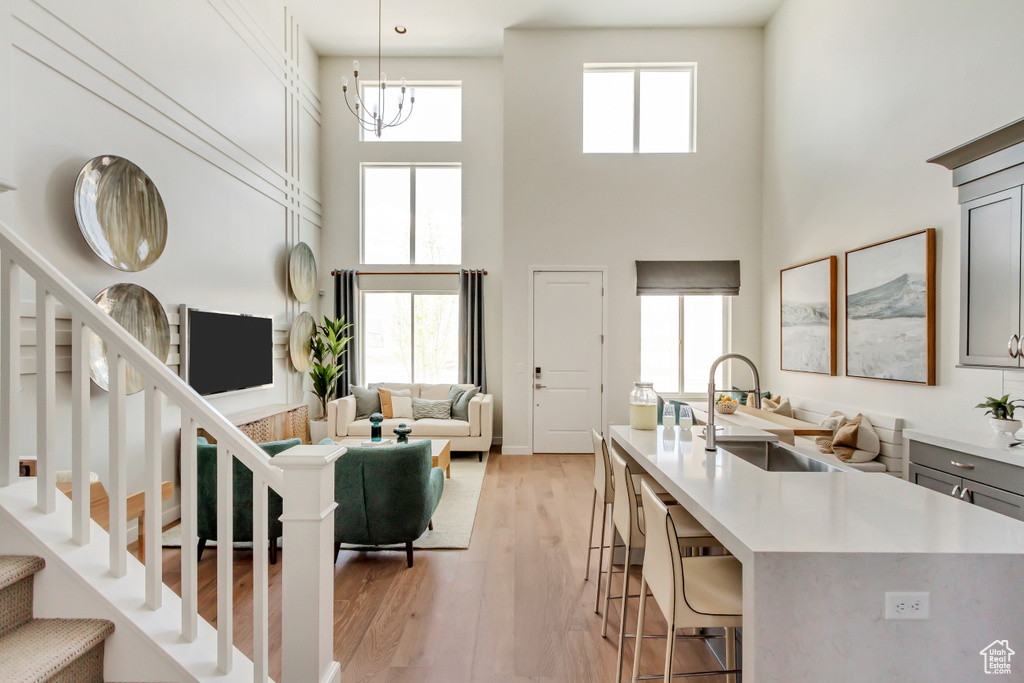 Living area with a high ceiling, stairs, light wood-style floors, and a chandelier