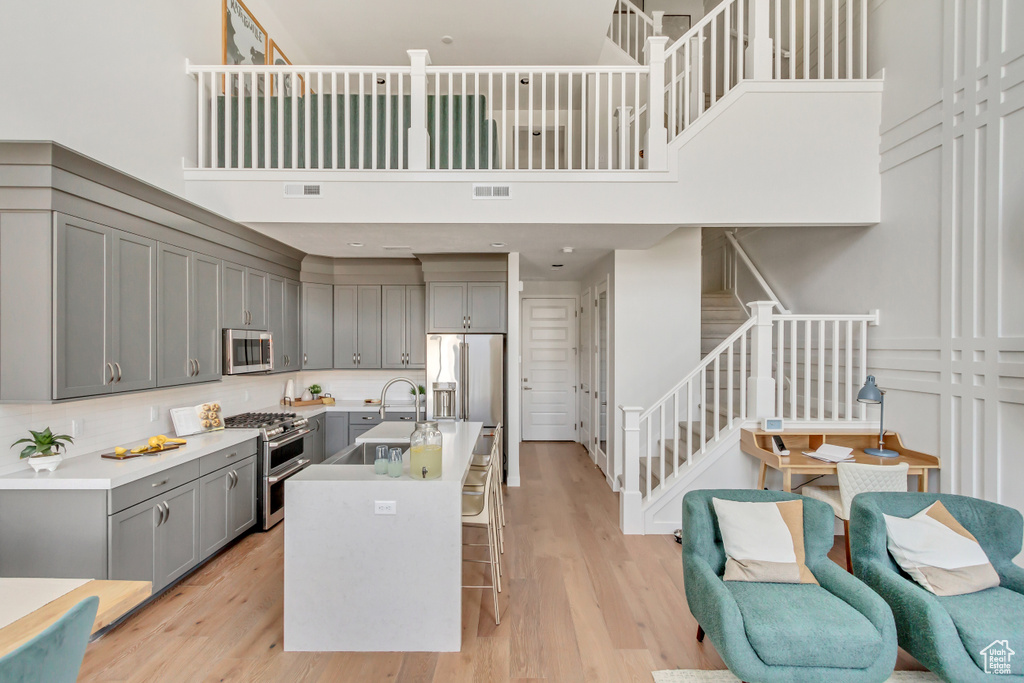 Kitchen featuring gray cabinets, appliances with stainless steel finishes, a high ceiling, light wood finished floors, and a kitchen bar