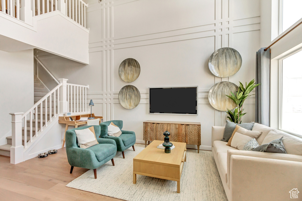 Living area featuring stairs, a decorative wall, healthy amount of natural light, wood finished floors, and a high ceiling