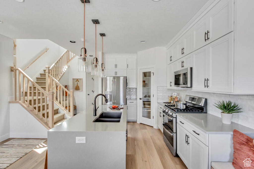 Kitchen featuring appliances with stainless steel finishes, light wood-style flooring, backsplash, a kitchen island with sink, and recessed lighting
