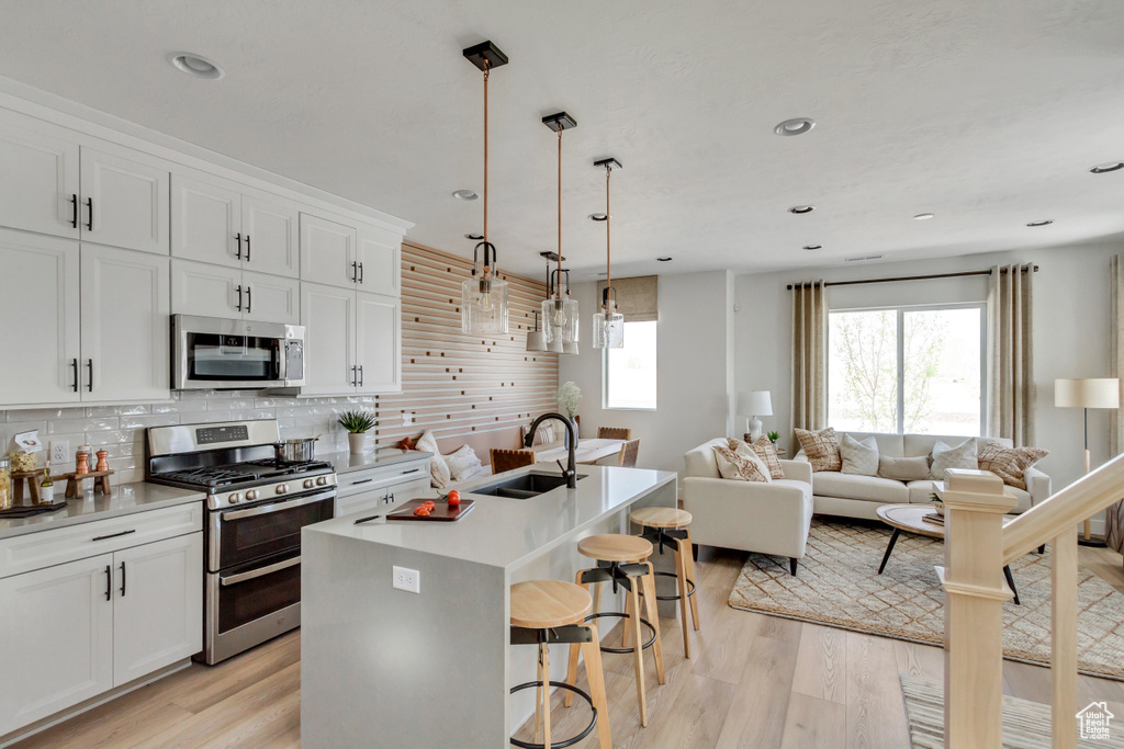 Kitchen featuring stainless steel appliances, light wood-style flooring, a breakfast bar area, open floor plan, and decorative backsplash