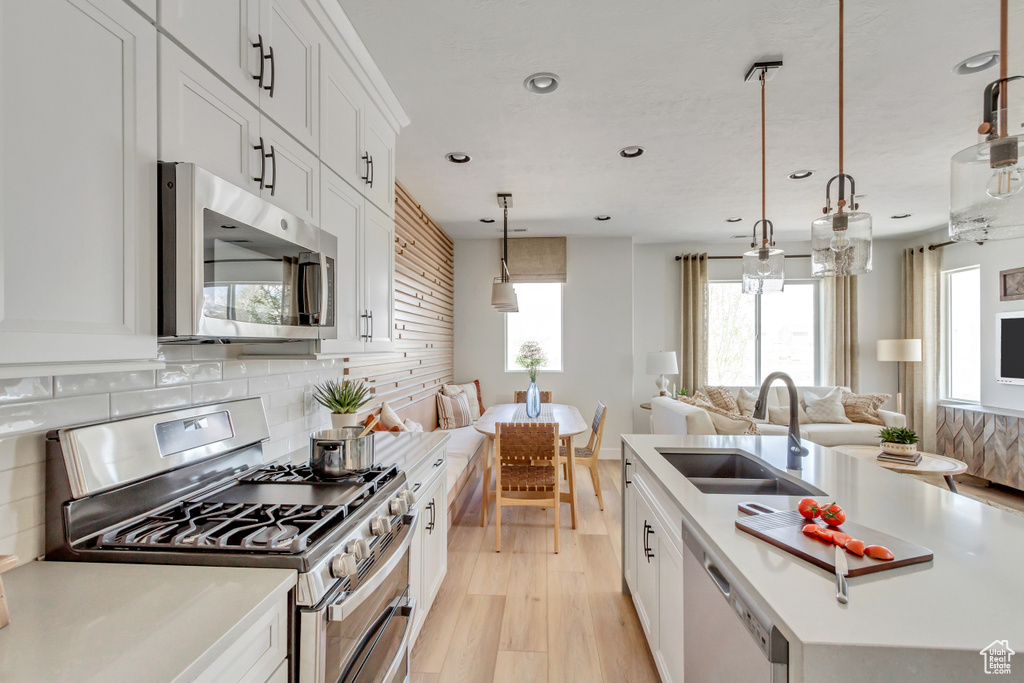 Kitchen with appliances with stainless steel finishes, recessed lighting, open floor plan, tasteful backsplash, and light wood-style floors
