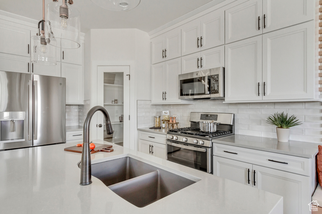 Kitchen with appliances with stainless steel finishes, white cabinets, tasteful backsplash, light countertops, and pendant lighting