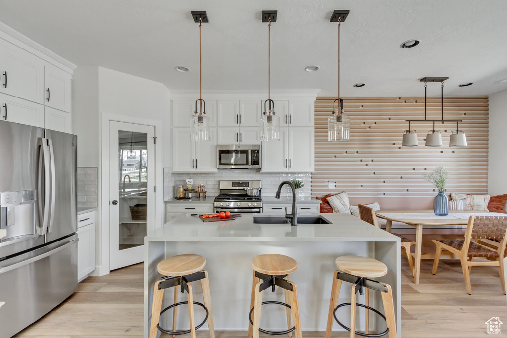 Kitchen featuring appliances with stainless steel finishes, light wood-type flooring, backsplash, a breakfast bar area, and recessed lighting