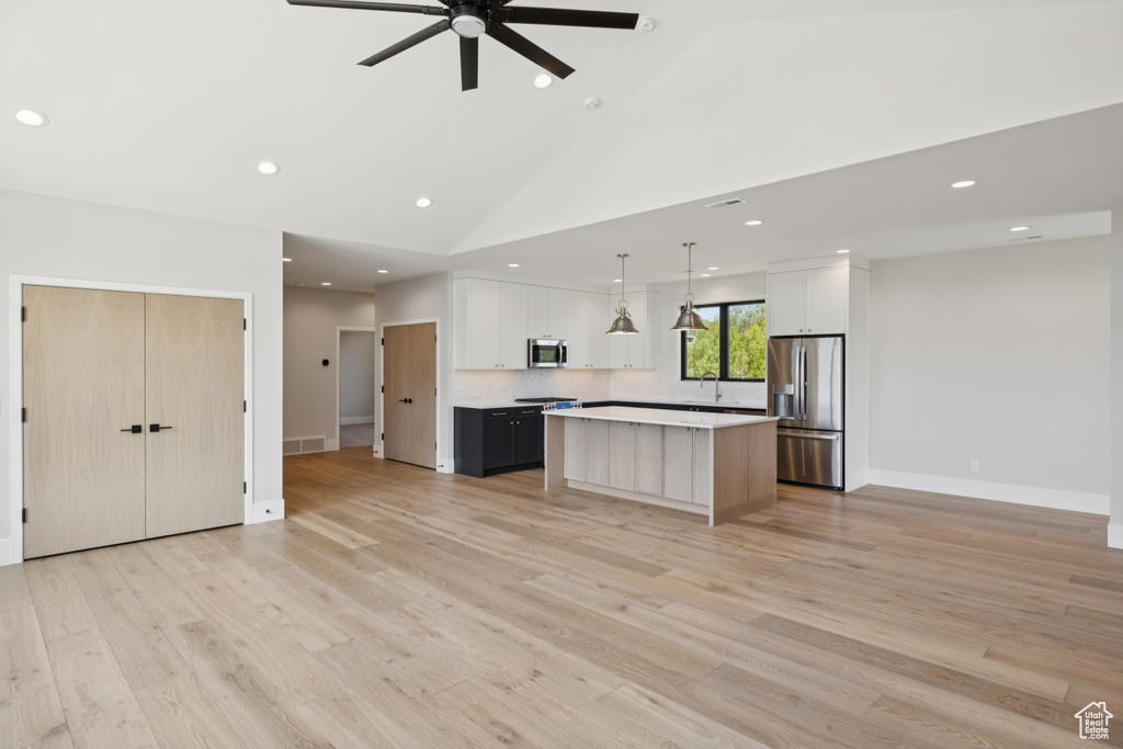 Kitchen featuring appliances with stainless steel finishes, a kitchen island, open floor plan, light countertops, and recessed lighting