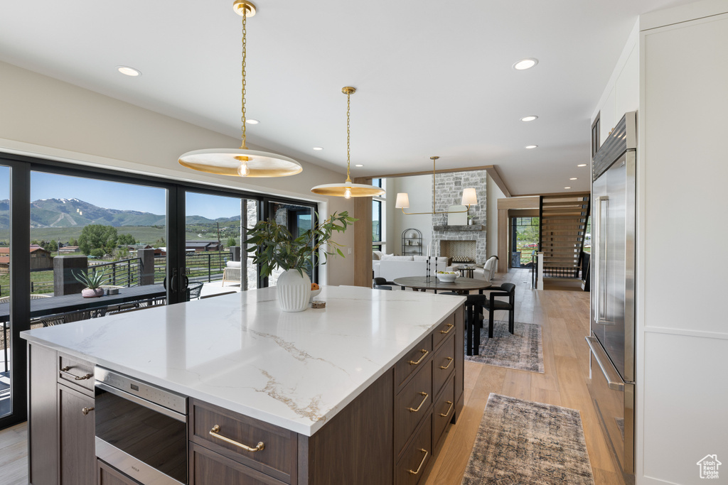 Kitchen featuring built in appliances, light wood-style floors, dark brown cabinetry, pendant lighting, and a kitchen island