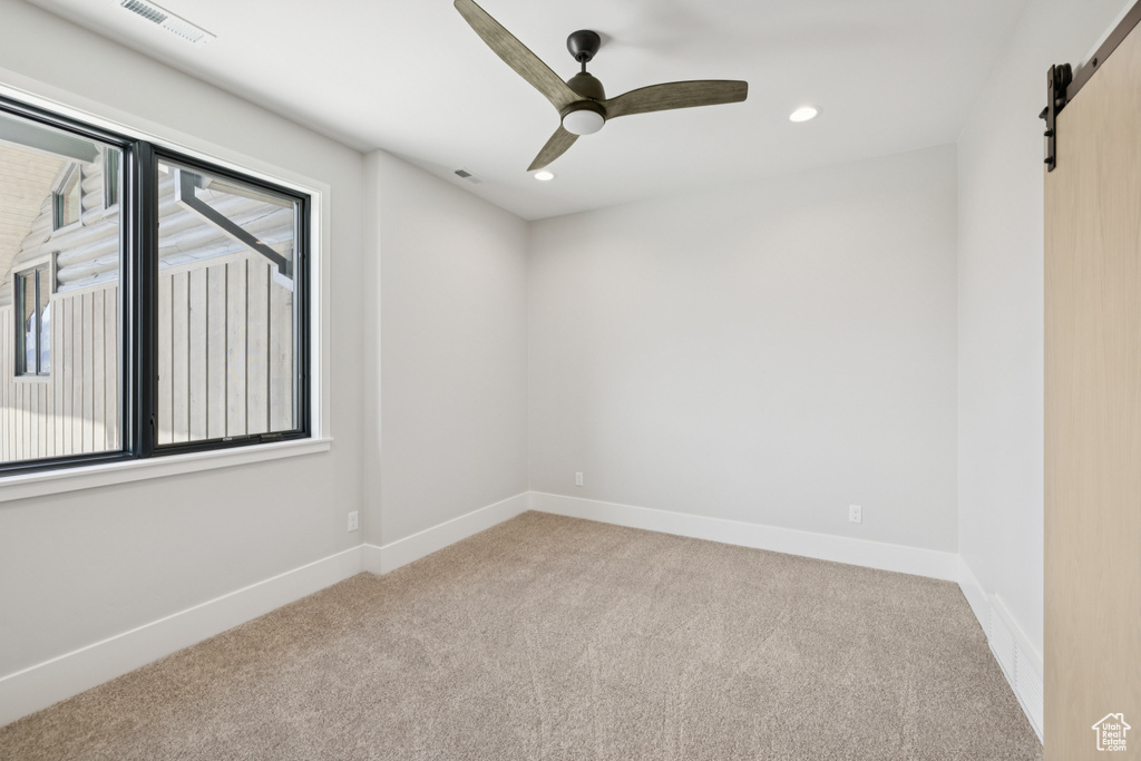 Carpeted spare room featuring a barn door, ceiling fan, and recessed lighting