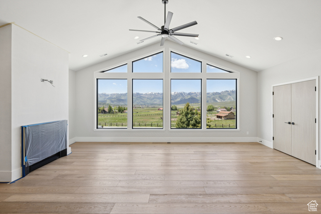 Unfurnished living room with ceiling fan, vaulted ceiling, light wood finished floors, a mountain view, and recessed lighting