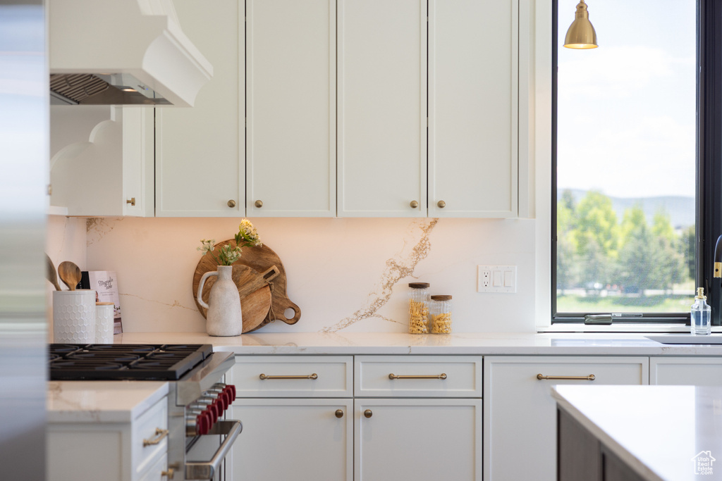 Kitchen with exhaust hood, stainless steel gas range oven, and white cabinetry