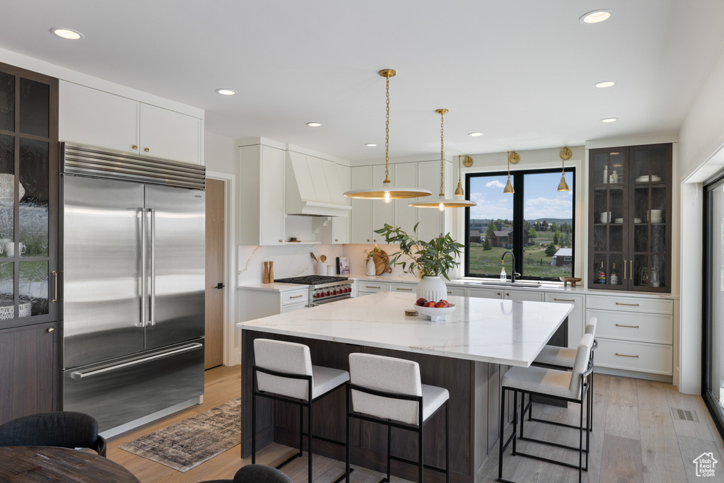 Kitchen with stainless steel built in refrigerator, custom range hood, light wood-style floors, a kitchen breakfast bar, and white cabinetry