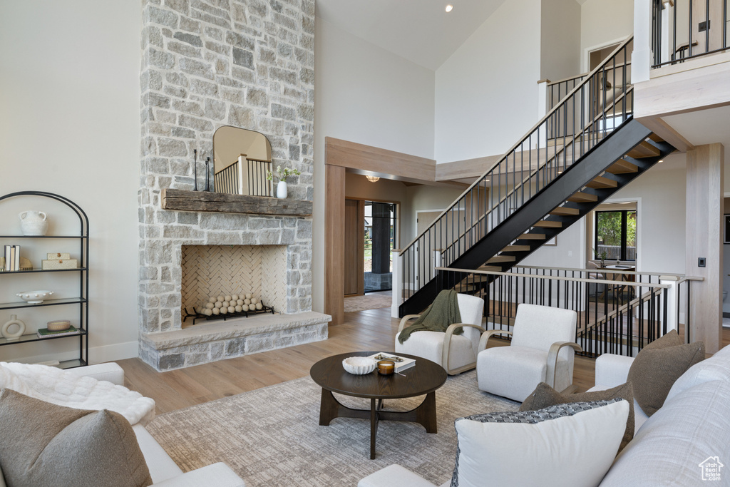 Living room with wood finished floors, plenty of natural light, high vaulted ceiling, a stone fireplace, and stairway