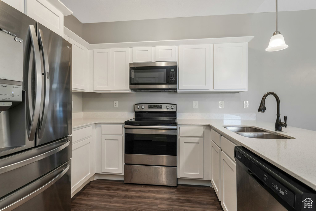 Kitchen with stainless steel appliances, white cabinetry, dark wood-type flooring, light stone countertops, and pendant lighting