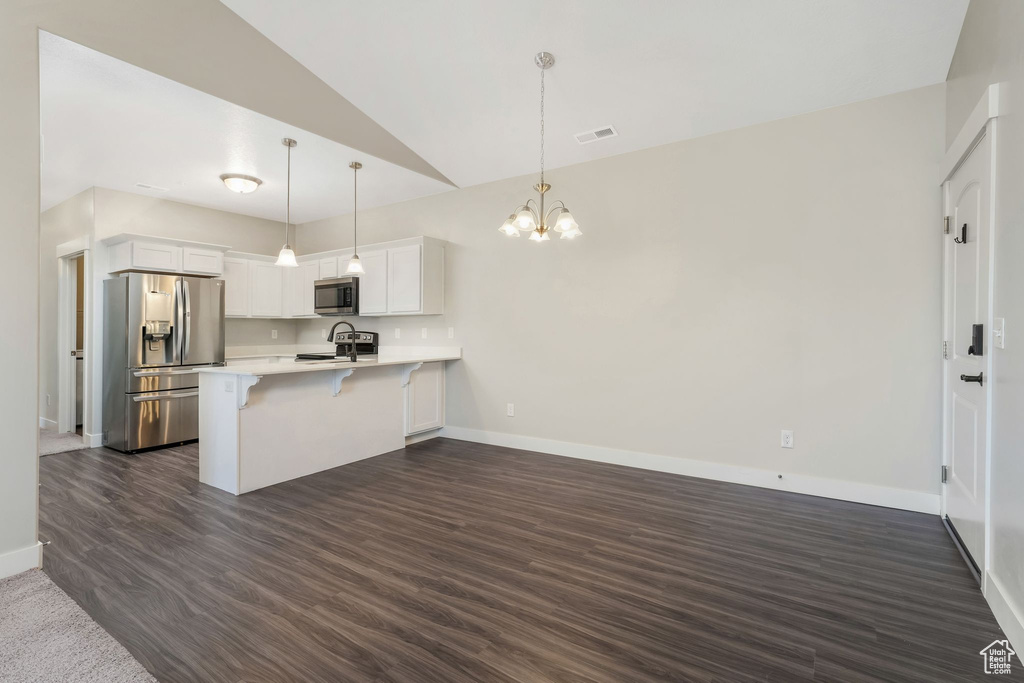 Kitchen with stainless steel appliances, a peninsula, light countertops, vaulted ceiling, and a kitchen bar