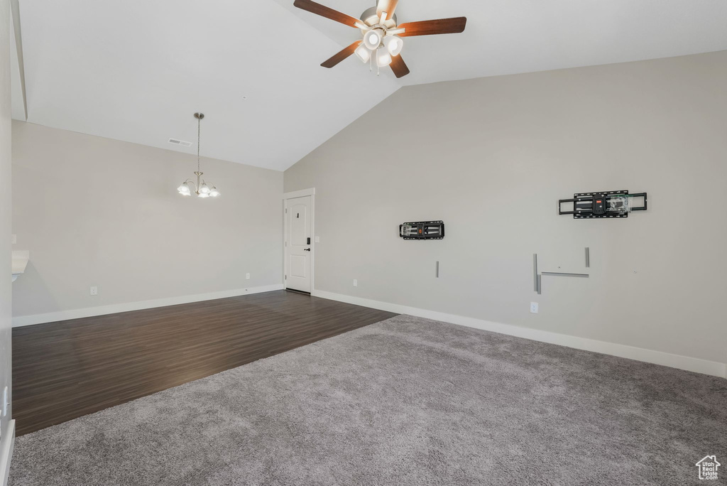 Unfurnished living room featuring ceiling fan, a chandelier, dark wood-type flooring, dark colored carpet, and high vaulted ceiling