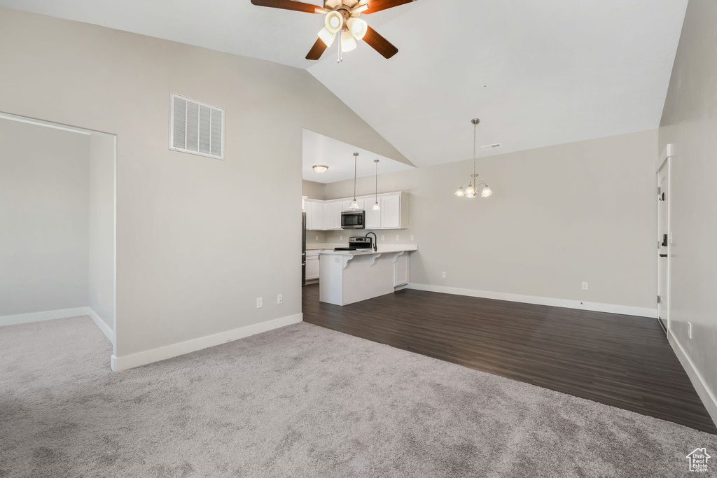 Unfurnished living room featuring ceiling fan, dark colored carpet, a chandelier, dark wood finished floors, and high vaulted ceiling