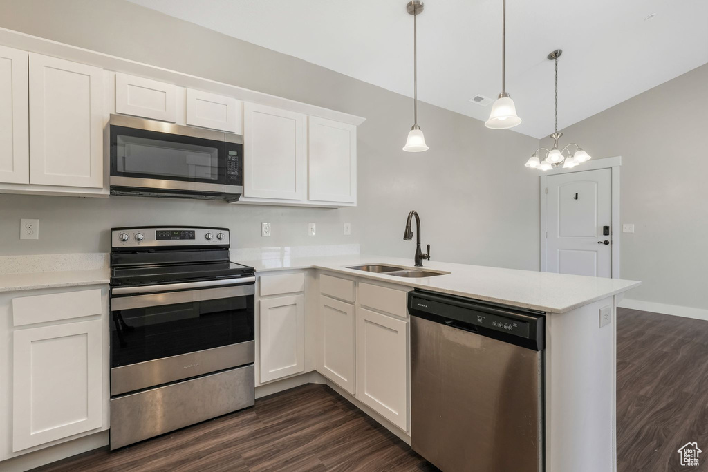 Kitchen with stainless steel appliances, a peninsula, dark wood finished floors, white cabinetry, and light countertops