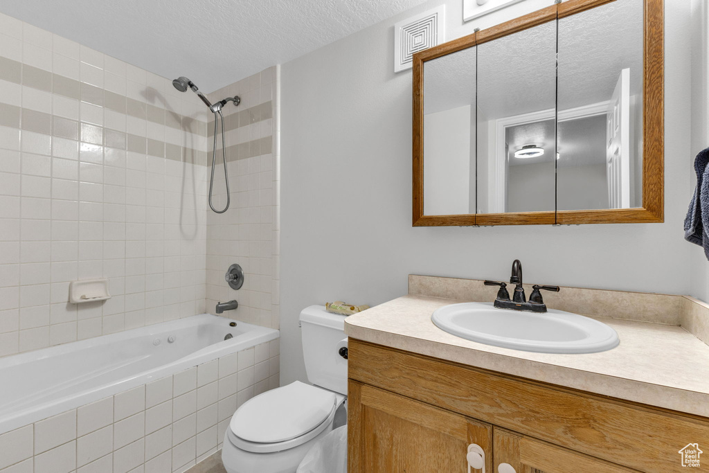 Bathroom featuring tiled shower / bath, vanity, and a textured ceiling