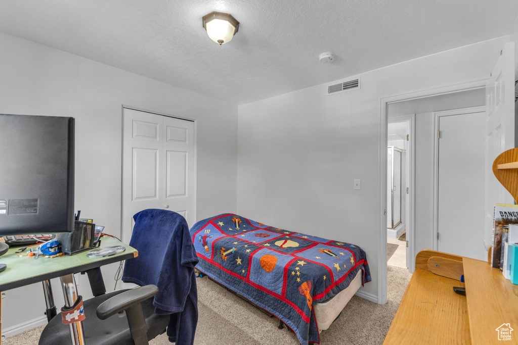 Carpeted bedroom featuring a textured ceiling, a closet, and an office area