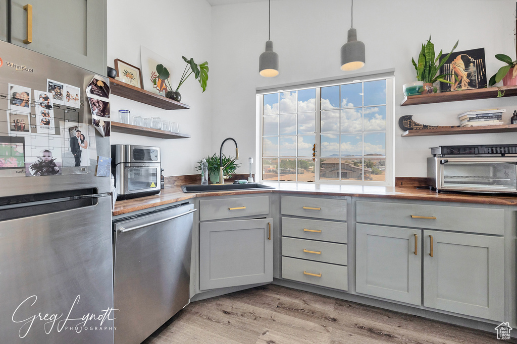 Kitchen with stainless steel appliances, open shelves, gray cabinets, light wood-style floors, and decorative light fixtures