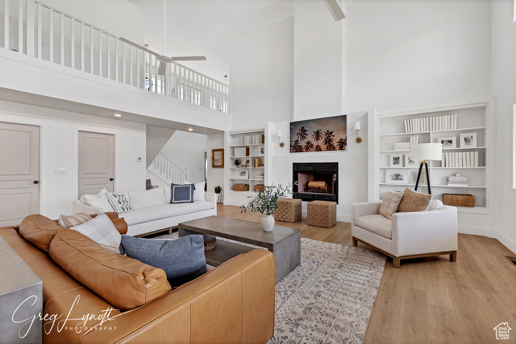 Living room featuring a high ceiling, light wood-style floors, stairs, a fireplace, and built in shelves