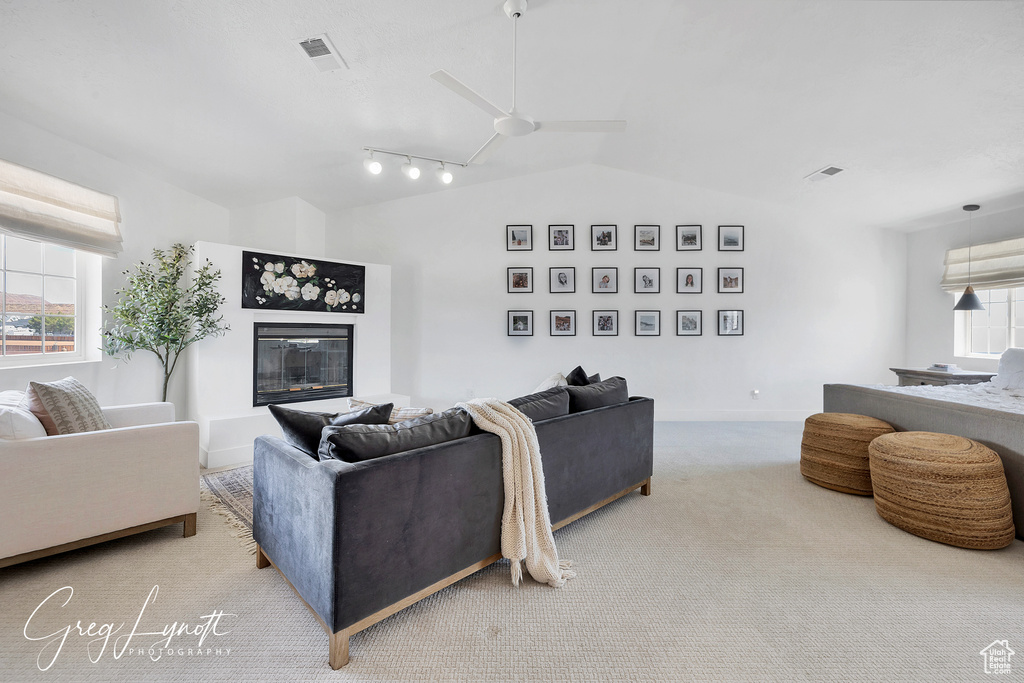 Carpeted living room featuring lofted ceiling, a glass covered fireplace, ceiling fan, and rail lighting