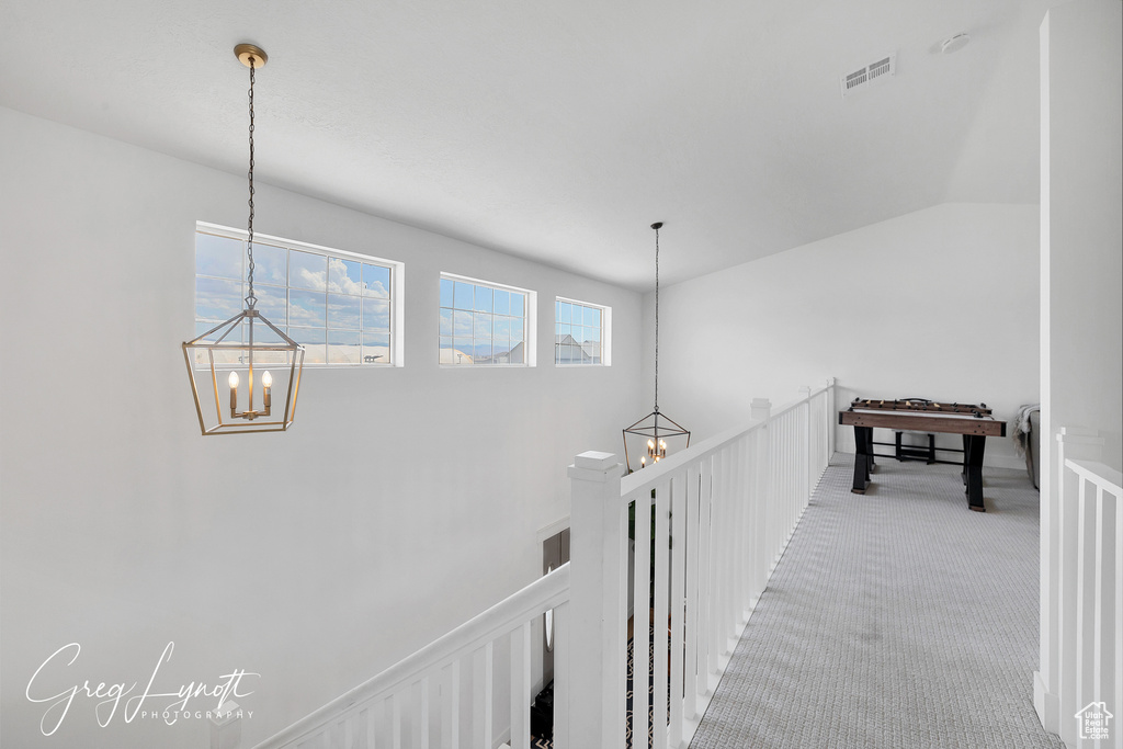 Hall with a chandelier, carpet floors, vaulted ceiling, and an upstairs landing
