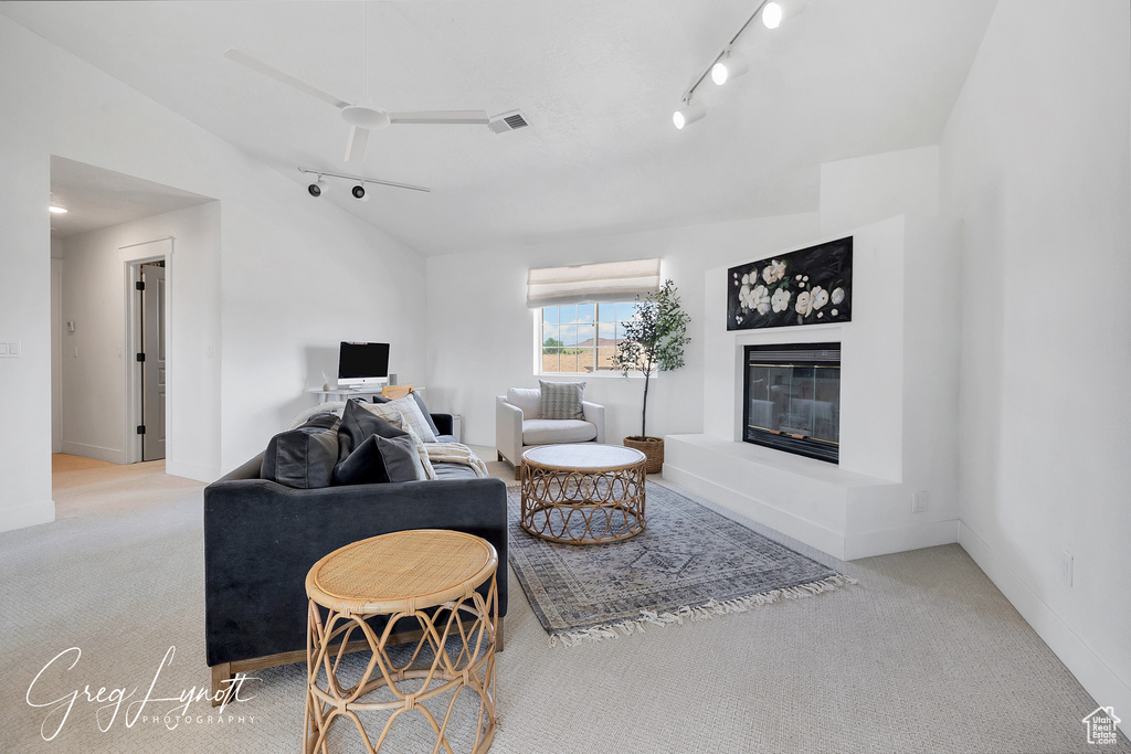 Living room with track lighting, carpet flooring, a glass covered fireplace, and lofted ceiling