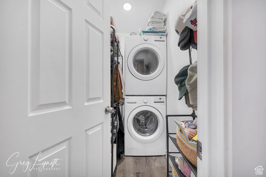 Laundry area with stacked washer / drying machine and wood finished floors