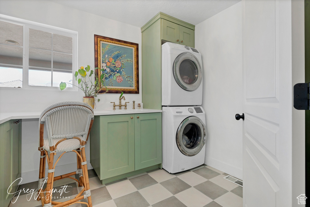 Laundry room featuring stacked washing machine and dryer, cabinet space, and light floors