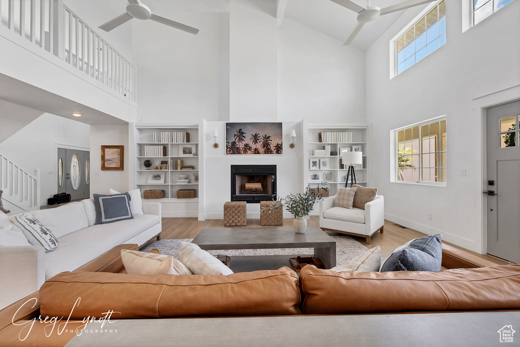 Living room featuring high vaulted ceiling, ceiling fan, wood finished floors, a fireplace, and beamed ceiling