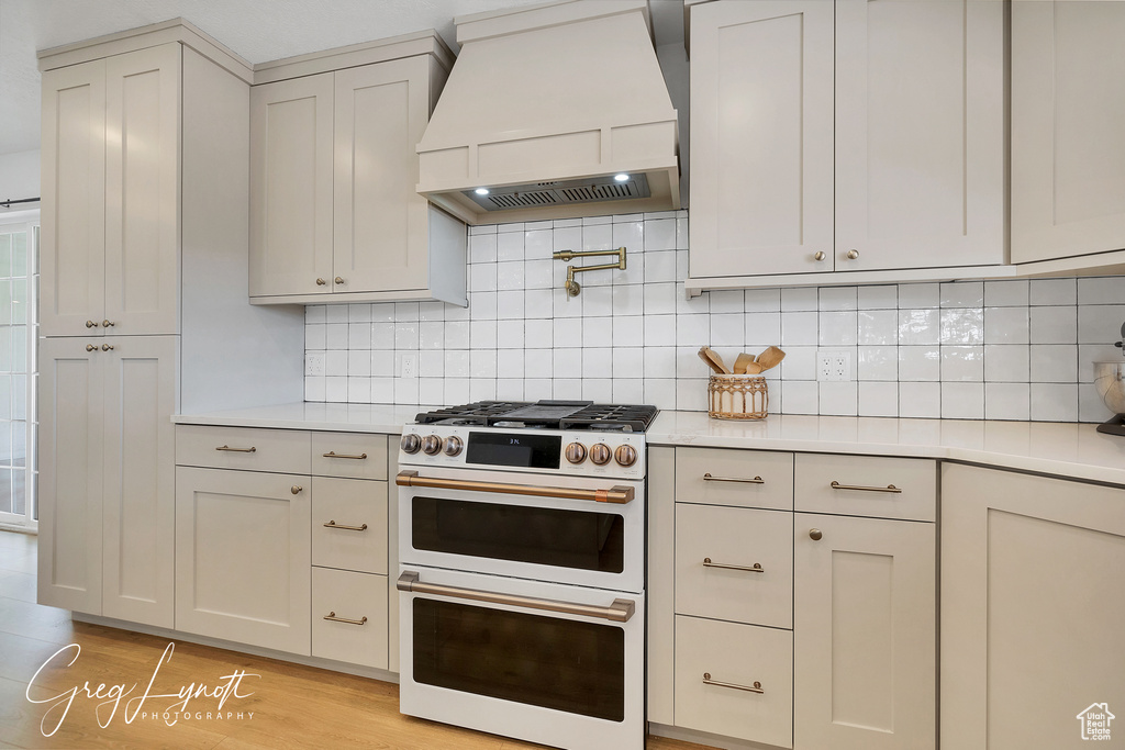 Kitchen with premium range hood, range with two ovens, light countertops, and light wood-style flooring