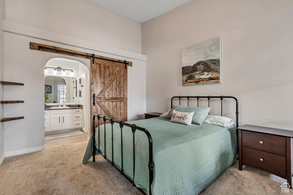 Bedroom with a barn door, arched walkways, light colored carpet, and ensuite bathroom
