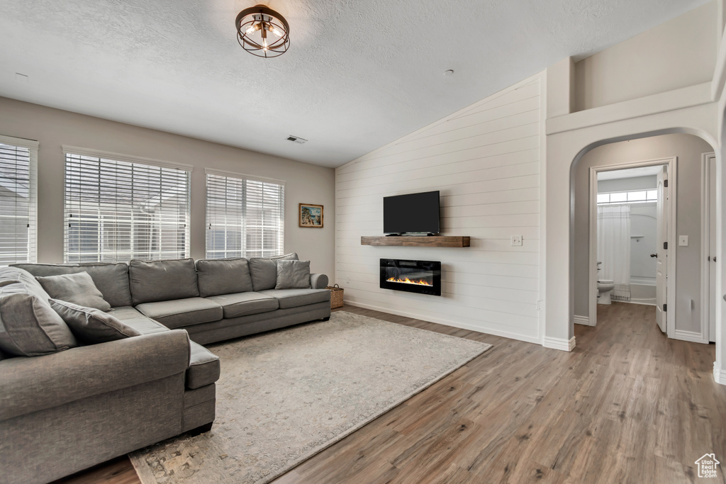 Living room featuring lofted ceiling, wood finished floors, a glass covered fireplace, a textured ceiling, and arched walkways